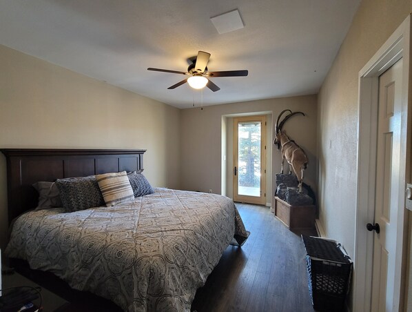 A bedroom with a large bed, a ceiling fan, a door with a view, and a mounted animal head.
