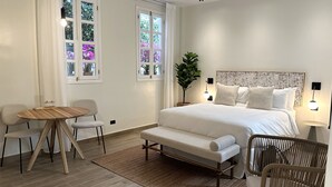 Een slaapkamer met een bed, nachtkastjes, een stoel, een klein tafeltje en een raam met gordijnen.