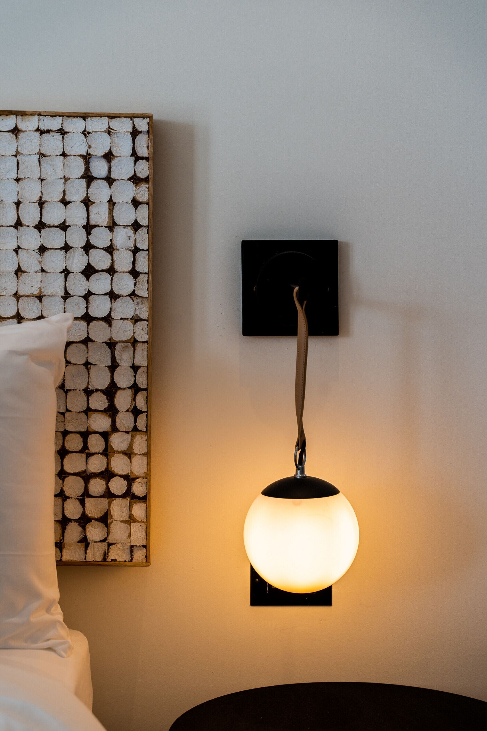 A wall-mounted light fixture with a spherical design and a square base, positioned above a wooden artwork with a grid pattern.