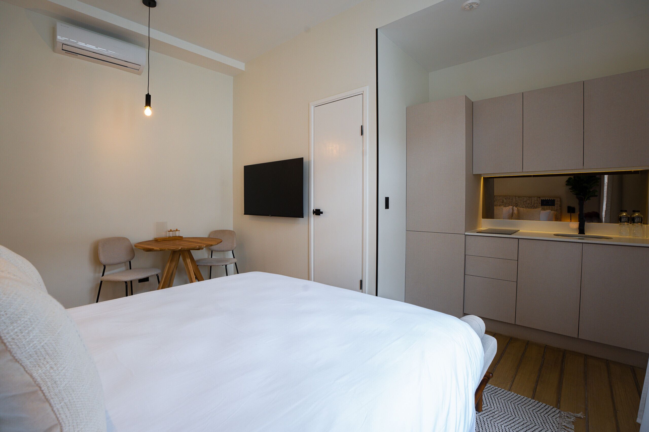 A bedroom with a bed, a small dining table, chairs, a TV, and a kitchenette.