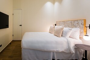 En pænt redt seng med hvide sengetøj og puder, et træhovedgærde og et natbord med en lampe.