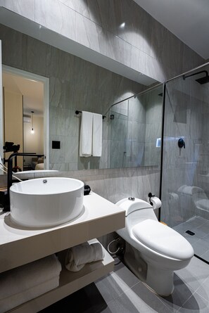 Et moderne badeværelse med et stort spejl, en rund vask, et toilet og en brusekabine i glas.
