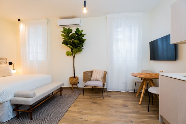 A modern bedroom with a bed, bench, chair, and a small dining table.