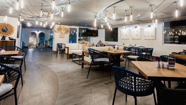 A modern restaurant with a curved ceiling, exposed wiring, and hanging light fixtures. Tables and chairs are arranged in a spacious layout. - HS HOTSSON Acapulco Villas (Acapulco)