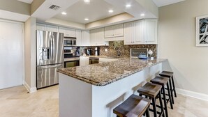 A modern kitchen with white cabinets, stainless steel appliances, and a granite countertop. - Heated Pool, Ocean Views, Pet-Friendly Paradise (Fernandina Beach)