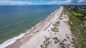 An aerial view of a beach with a long stretch of sand, a few umbrellas, and buildings in the background. - Heated Pool, Ocean Views, Pet-Friendly Paradise (Fernandina Beach)