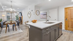 Uma cozinha moderna com uma ilha central, uma área de refeições com mesa e cadeiras, e uma porta de madeira.
