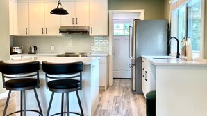 A modern kitchen with white cabinets, a stainless steel refrigerator, and a bar area with stools.