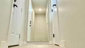 A narrow, well-lit hallway with white walls and wooden steps leading to a door at the end.