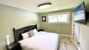 A bedroom with a bed, nightstands, a ceiling light, a window, and a TV mounted on the wall.