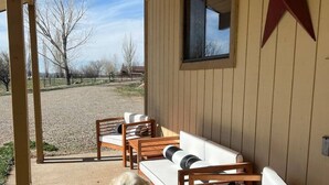 A covered patio with a row of wooden chairs and a white sofa, a red star decoration on the wall, and a dog sitting on the patio. - Starlight Casita Durango (Durango)
