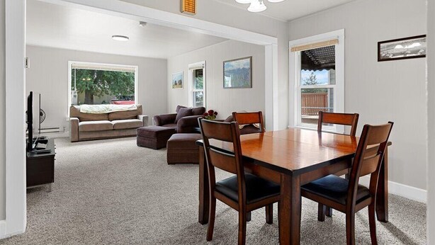 A spacious living room with a large wooden dining table, comfortable seating, and a view of the outdoors. - Cozy Cowboy Cabin in Polson: Historic Charm, Modern Comfort Near Flathead Lake (Polson)