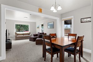 A spacious living room with a large wooden dining table, comfortable seating, and a view of the outdoors.