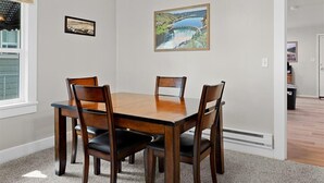 A dining room with a wooden table and chairs, a framed picture on the wall, and a window with blinds. - Cozy Cowboy Cabin in Polson: Historic Charm, Modern Comfort Near Flathead Lake (Polson)