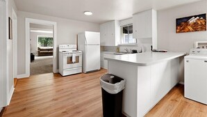 A modern kitchen with white cabinetry, a central island, and a view into the adjacent living room. - Cozy Cowboy Cabin in Polson: Historic Charm, Modern Comfort Near Flathead Lake (Polson)