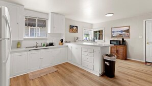 A modern kitchen with white cabinetry, a built-in oven, and a microwave. There is a window with a view of the outdoors, and a trash can is visible. - Cozy Cowboy Cabin in Polson: Historic Charm, Modern Comfort Near Flathead Lake (Polson)
