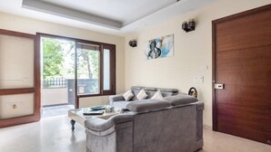 A living room with a grey sofa, a coffee table, and a painting on the wall. - Cozy Getaway: Clean and modern!!!    Breakfast Included !! (Gurugram)