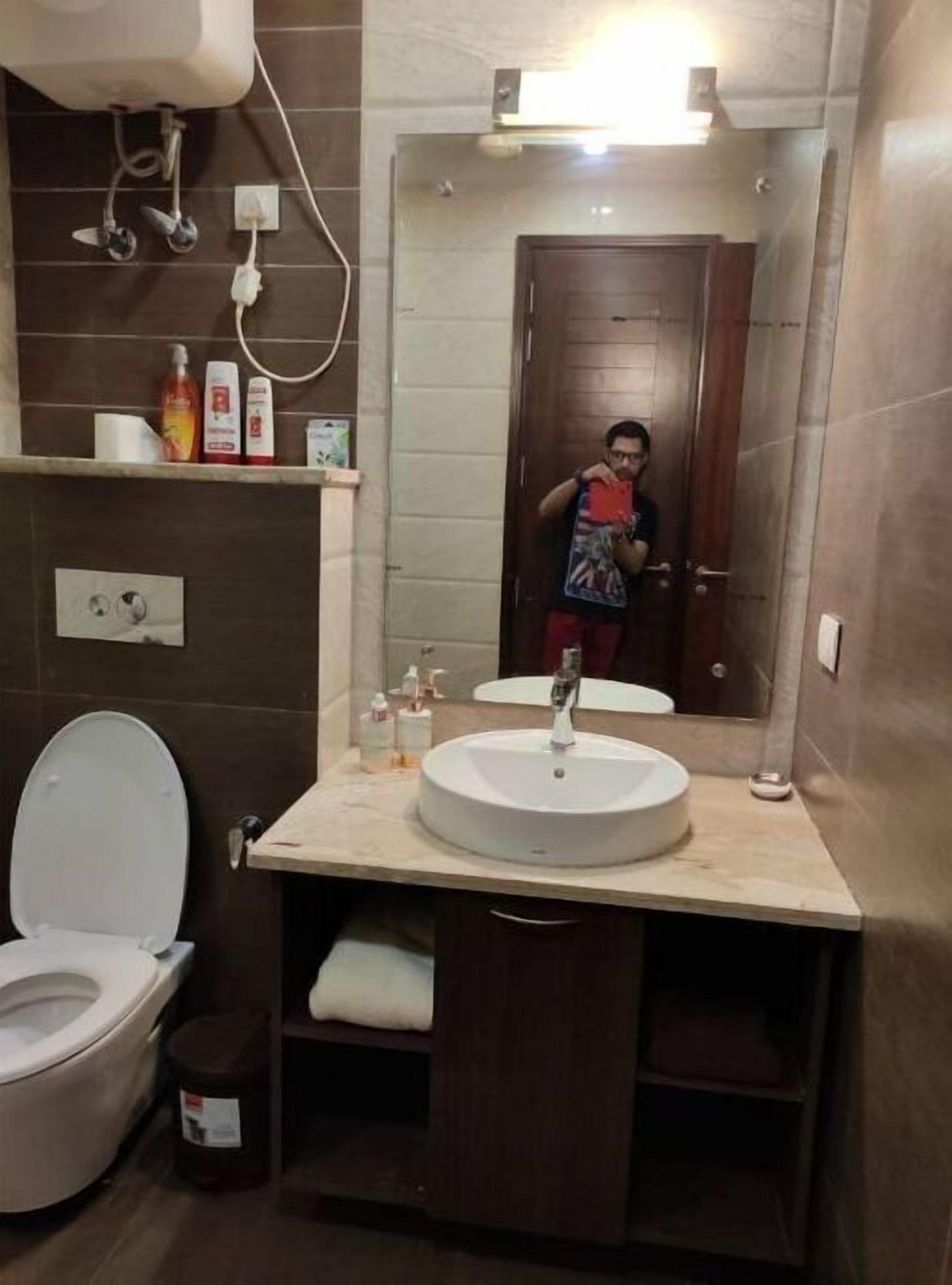 Une salle de bain équipée de toilettes, d’un lavabo et d’un miroir. On trouve des articles de toilette sur l’étagère au-dessus du lavabo.