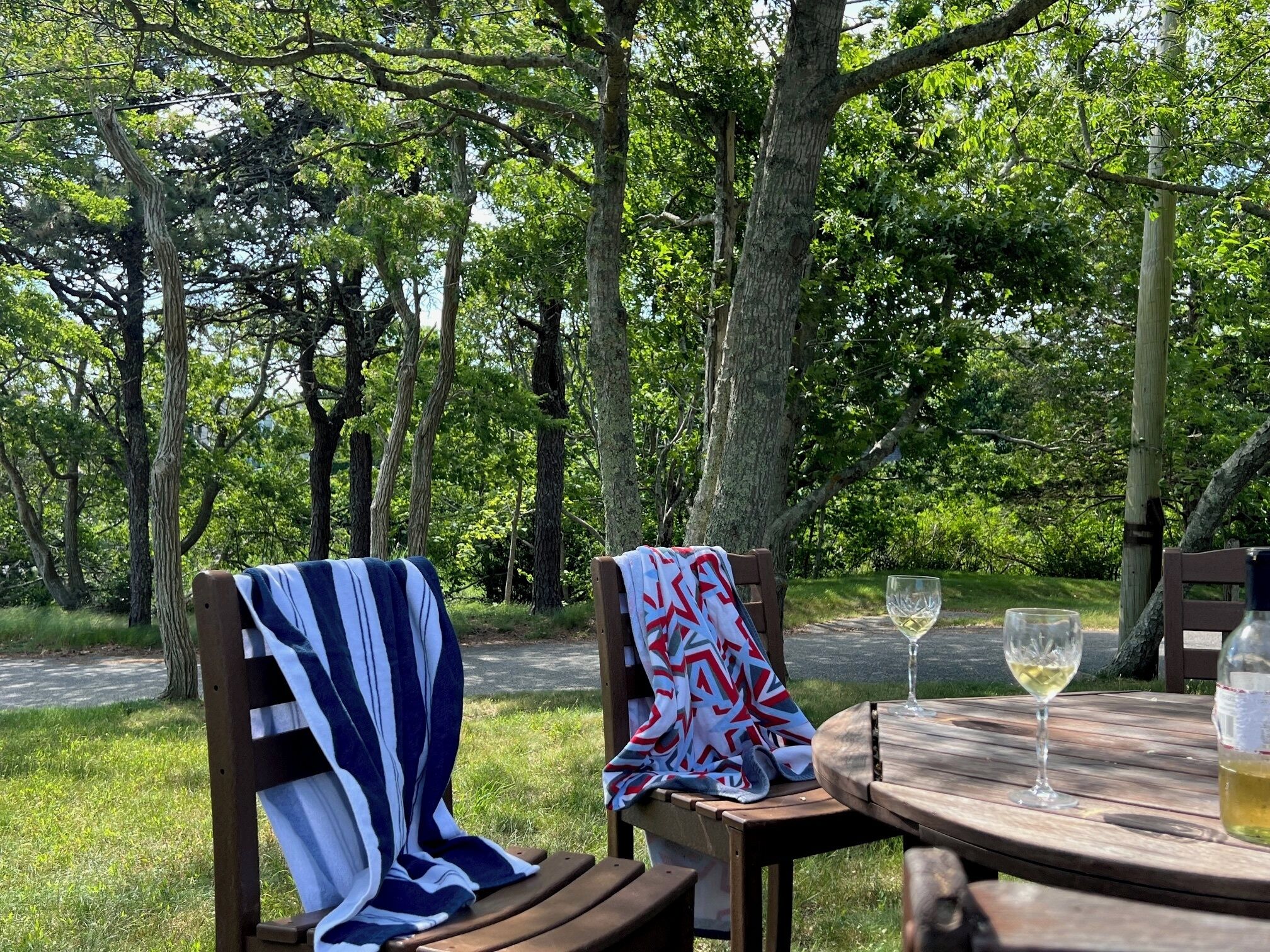 A wooden bench with a striped blanket, a table with a wine glass and a bottle, and a view of a forested area.