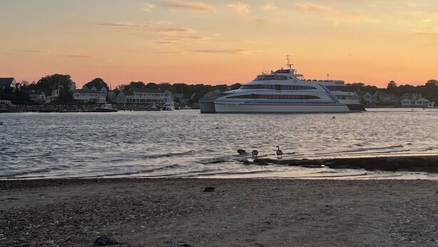 Eine große Yacht liegt in einer Marina vor einer Küste.