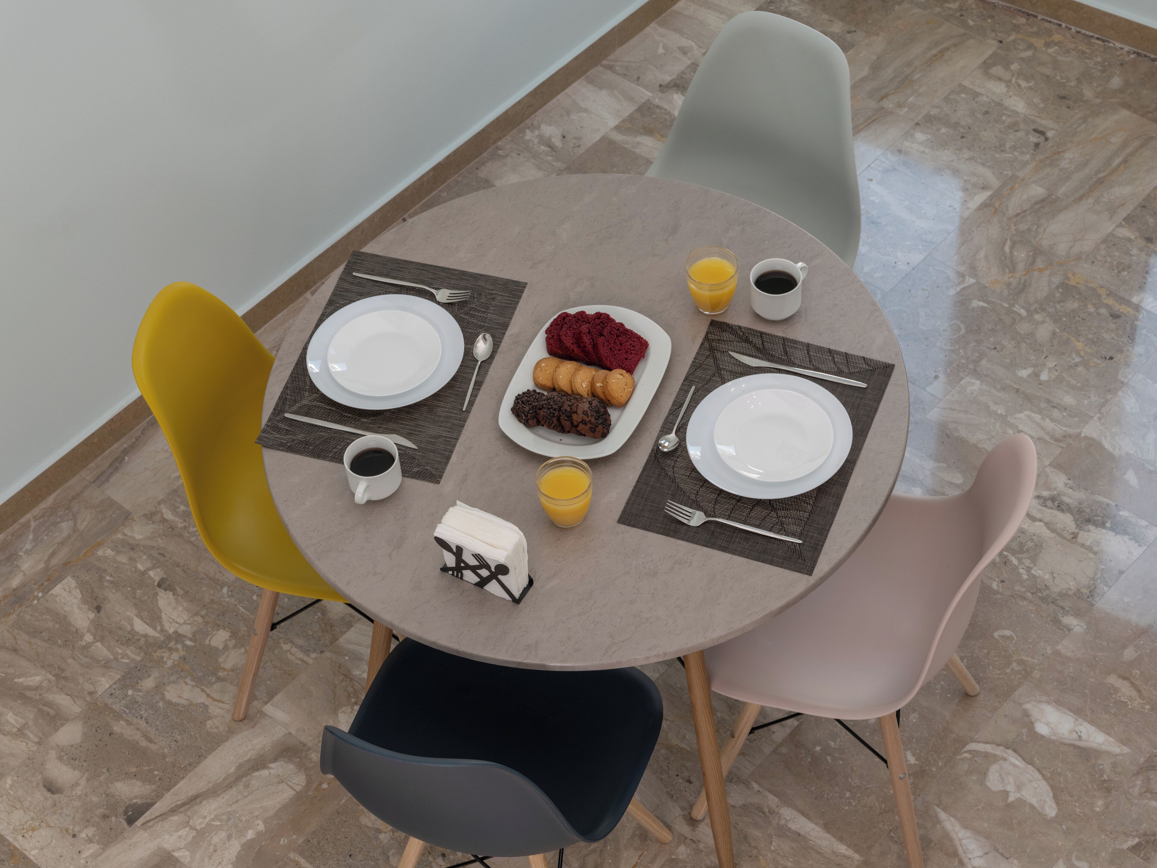 A dining table set with plates, cutlery, and a coffee cup, surrounded by colorful chairs.