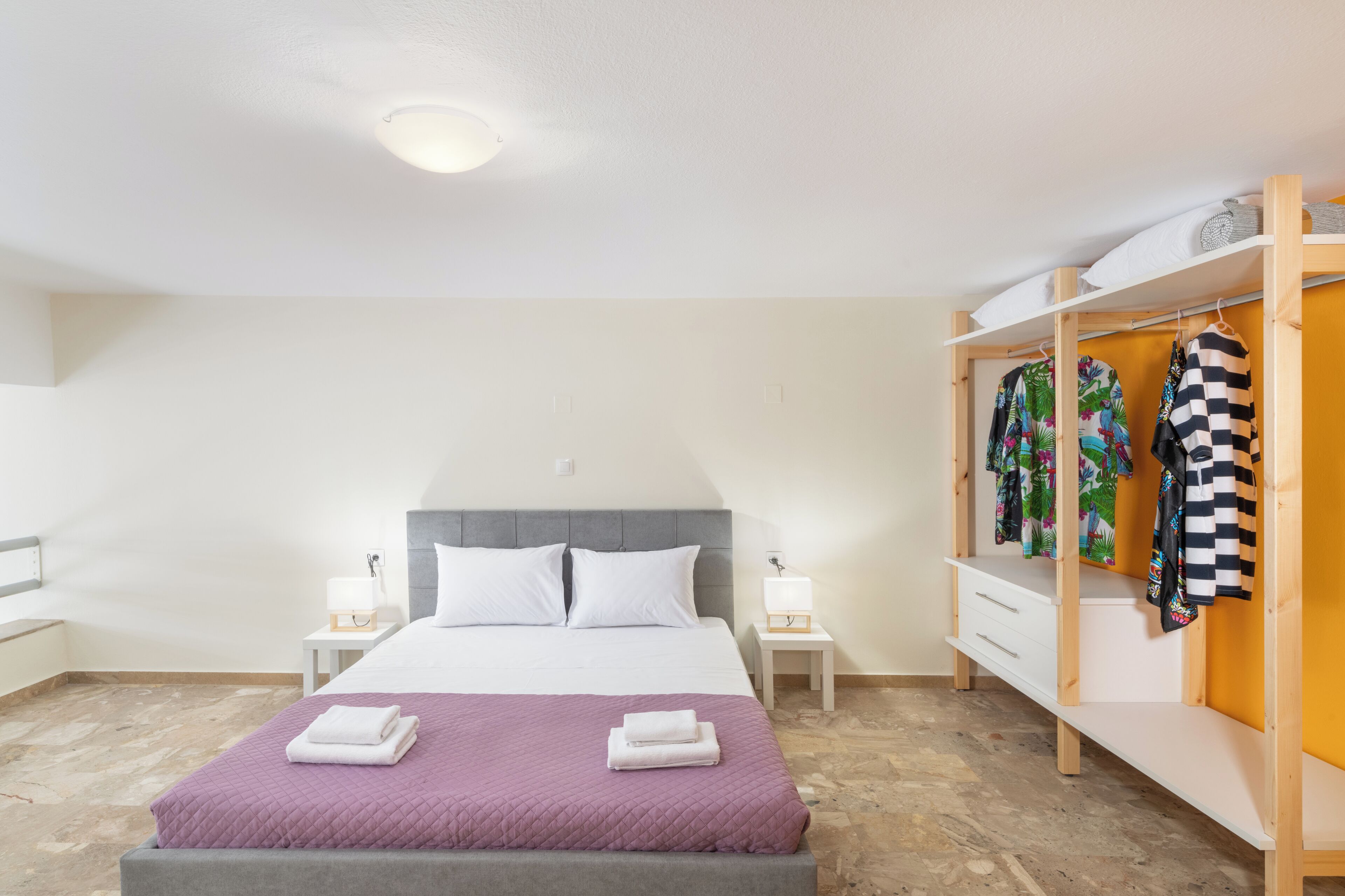 A neatly arranged bedroom with a bed, bedside tables, a wardrobe, and a hanging rack.