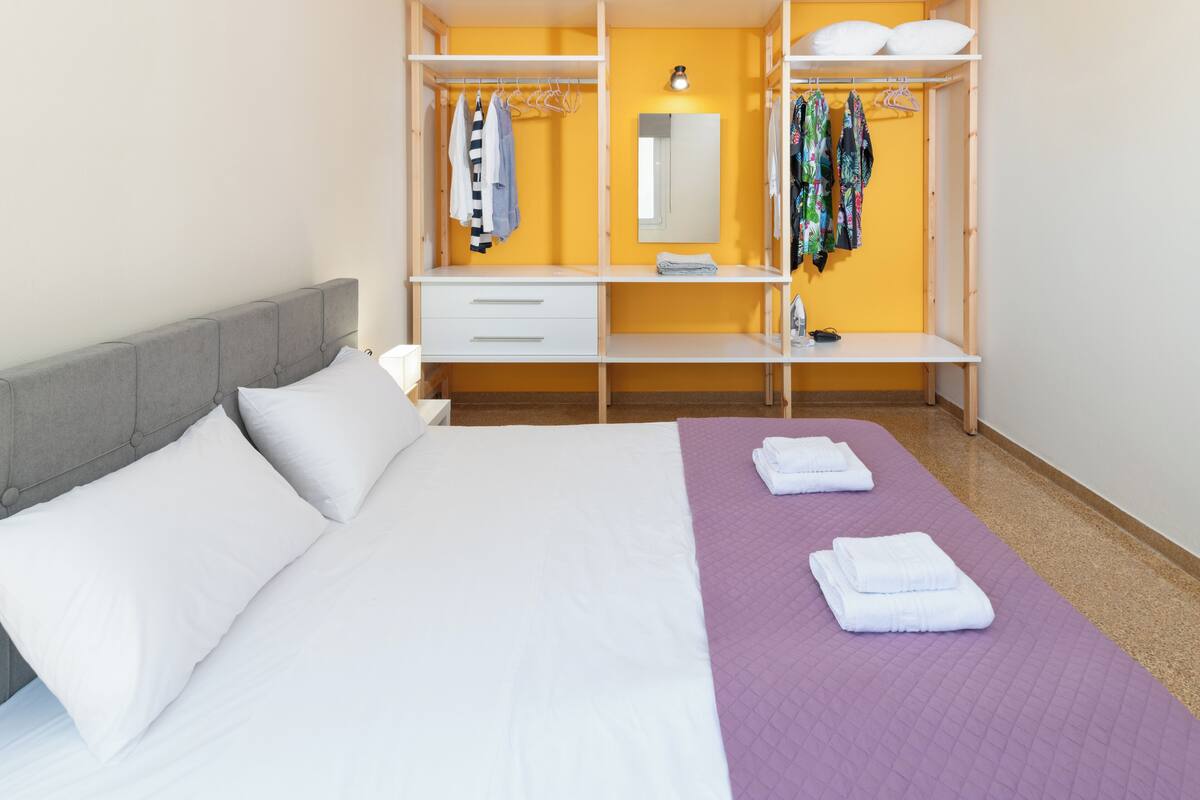 Een hotelkamer met een bed, nachtkastje, kledingkast en spiegel.