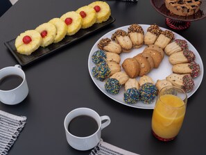 Una mesa con un plato de galletas, un plato de rodajas de piña, dos tazas de café y un vaso de jugo de naranja.