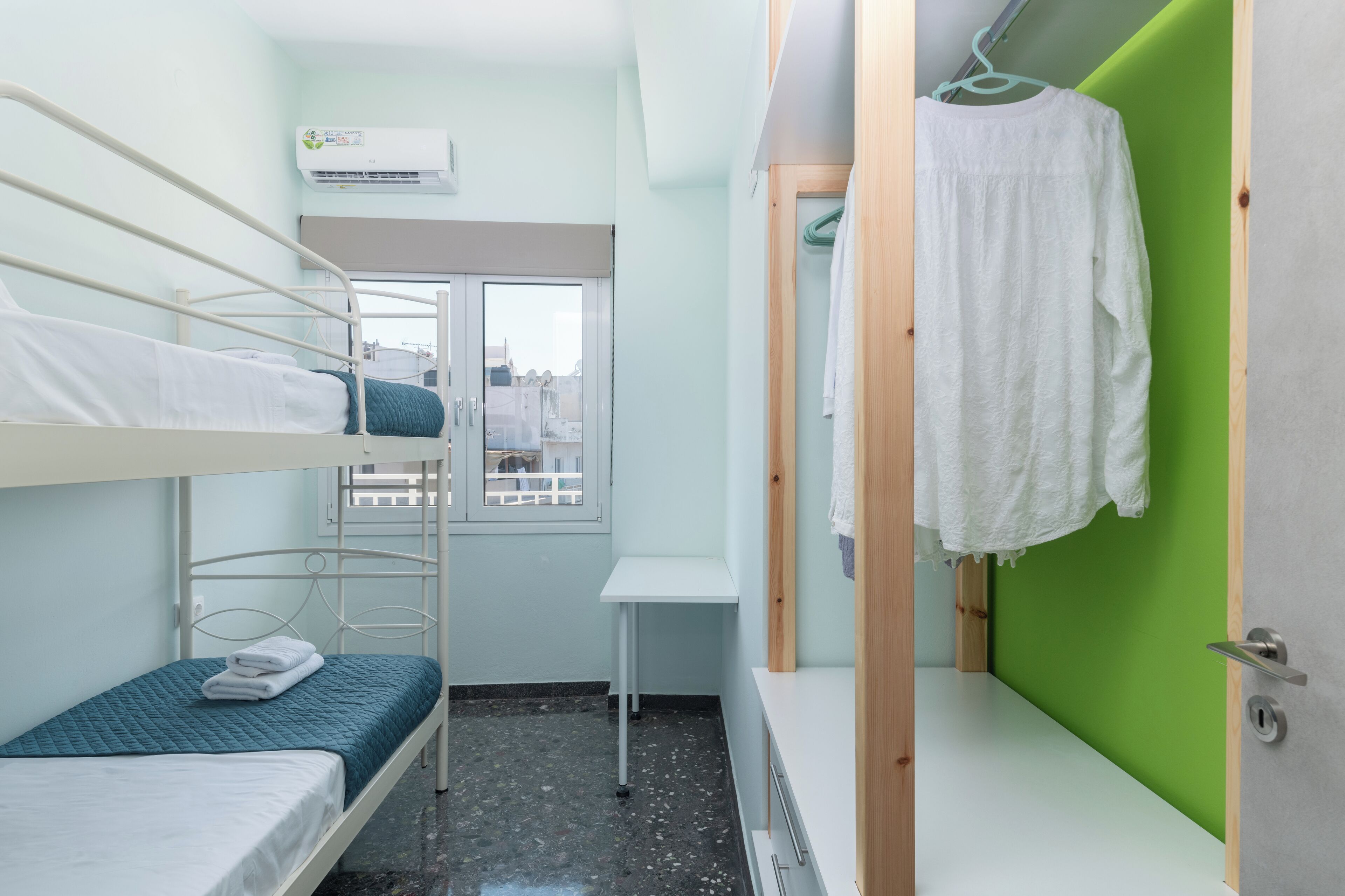 Une chambre de dortoir avec des lits superposés, une petite table, une fenêtre et un mur vert.