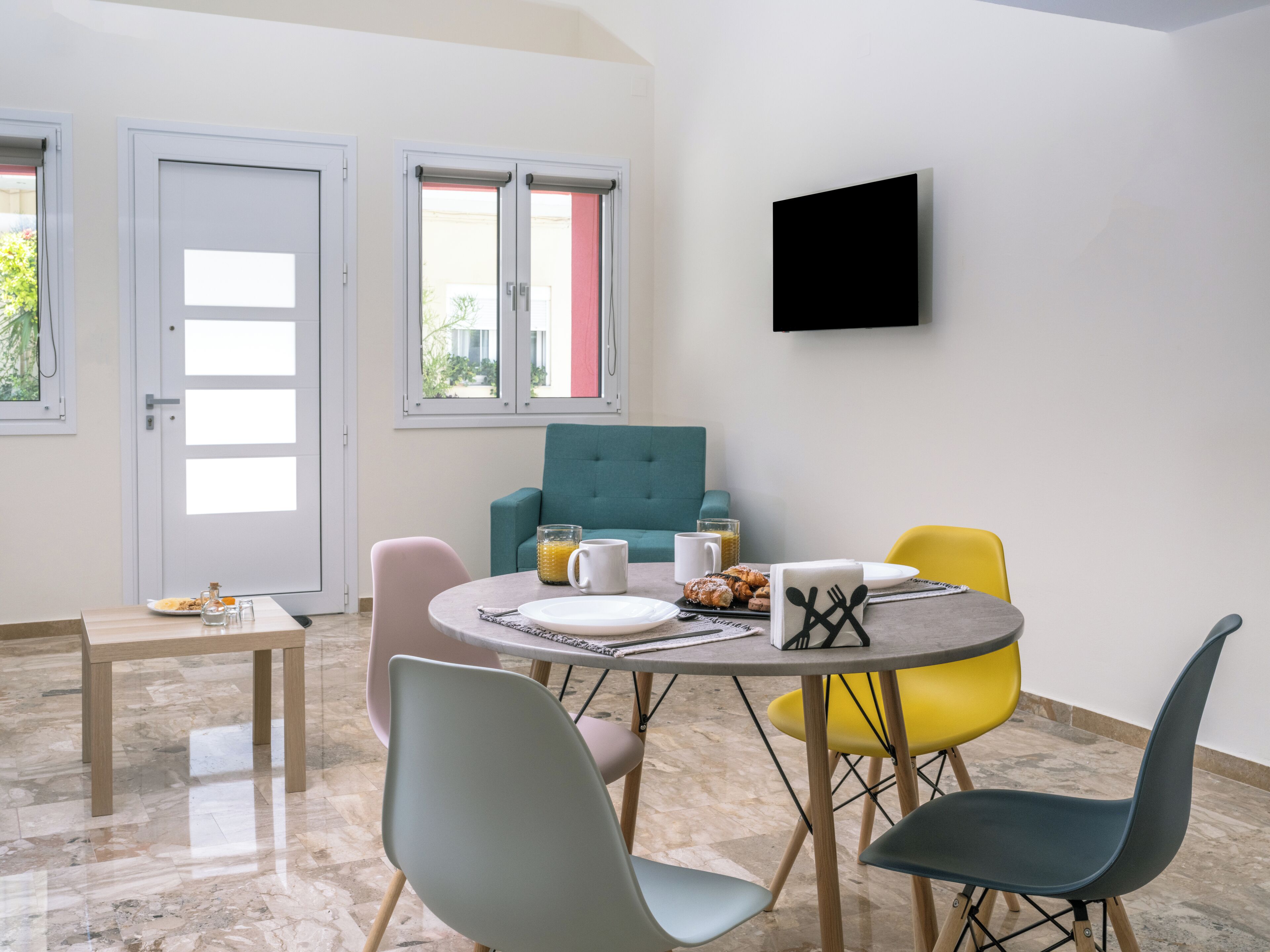 A modern dining area with a round table, colorful chairs, and a teal sofa.