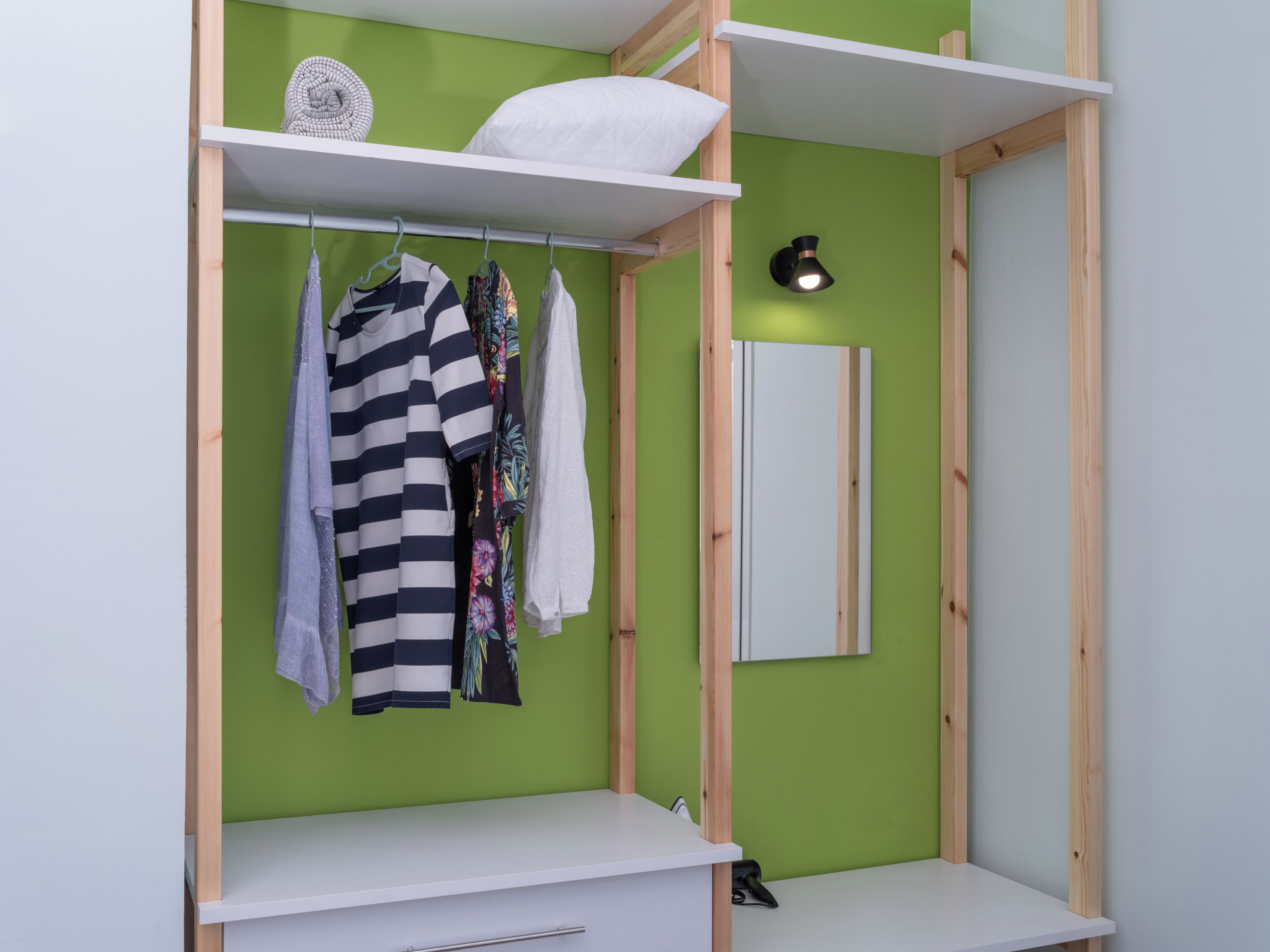 Une pièce avec un mur vert, une étagère blanche et un portant à vêtements suspendu.