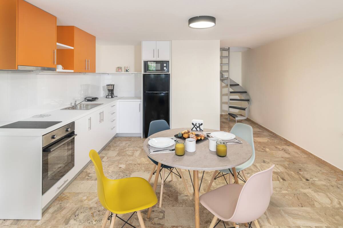 Een moderne keuken met witte en oranje kastjes, een zwarte koelkast, en een eethoek met een ronde tafel en twee stoelen.