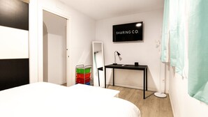 Hotellihuone, jossa on sänky, työpöytä, peili, televisio ja säilytystila.