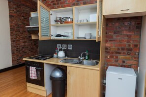 Una cocina compacta con pared de ladrillo, armarios de madera, estufa, lavamanos y un refrigerador pequeño.