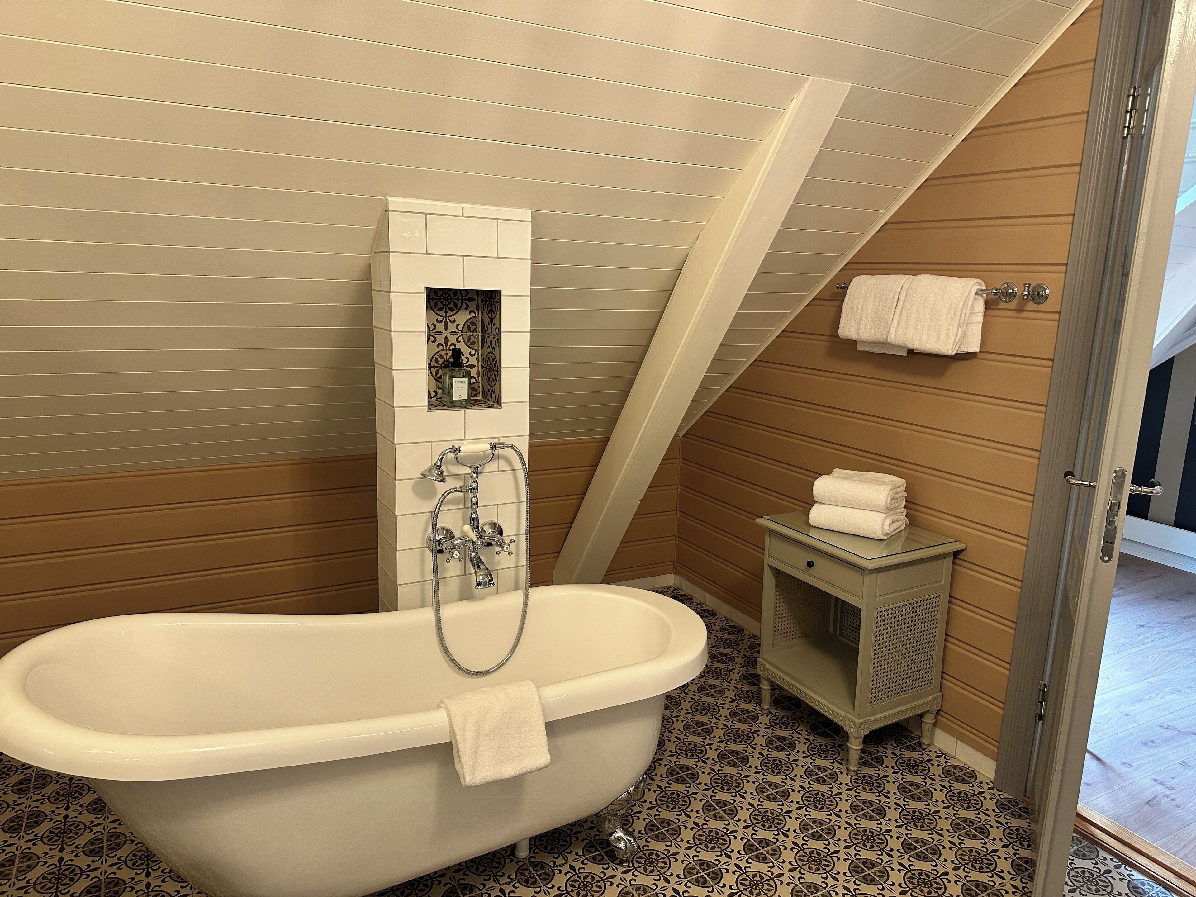 Un bagno con una vasca freestanding, un piccolo mobile lavabo con specchio e un portascopevoli.