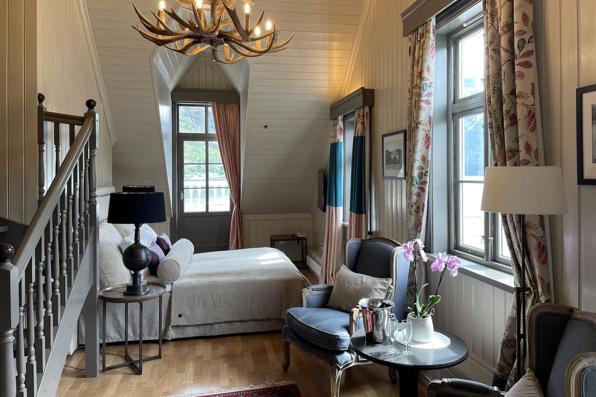 Un cuarto acogedor con cama, una silla, una mesita con lámpara, un candelabro y una ventana con cortinas.