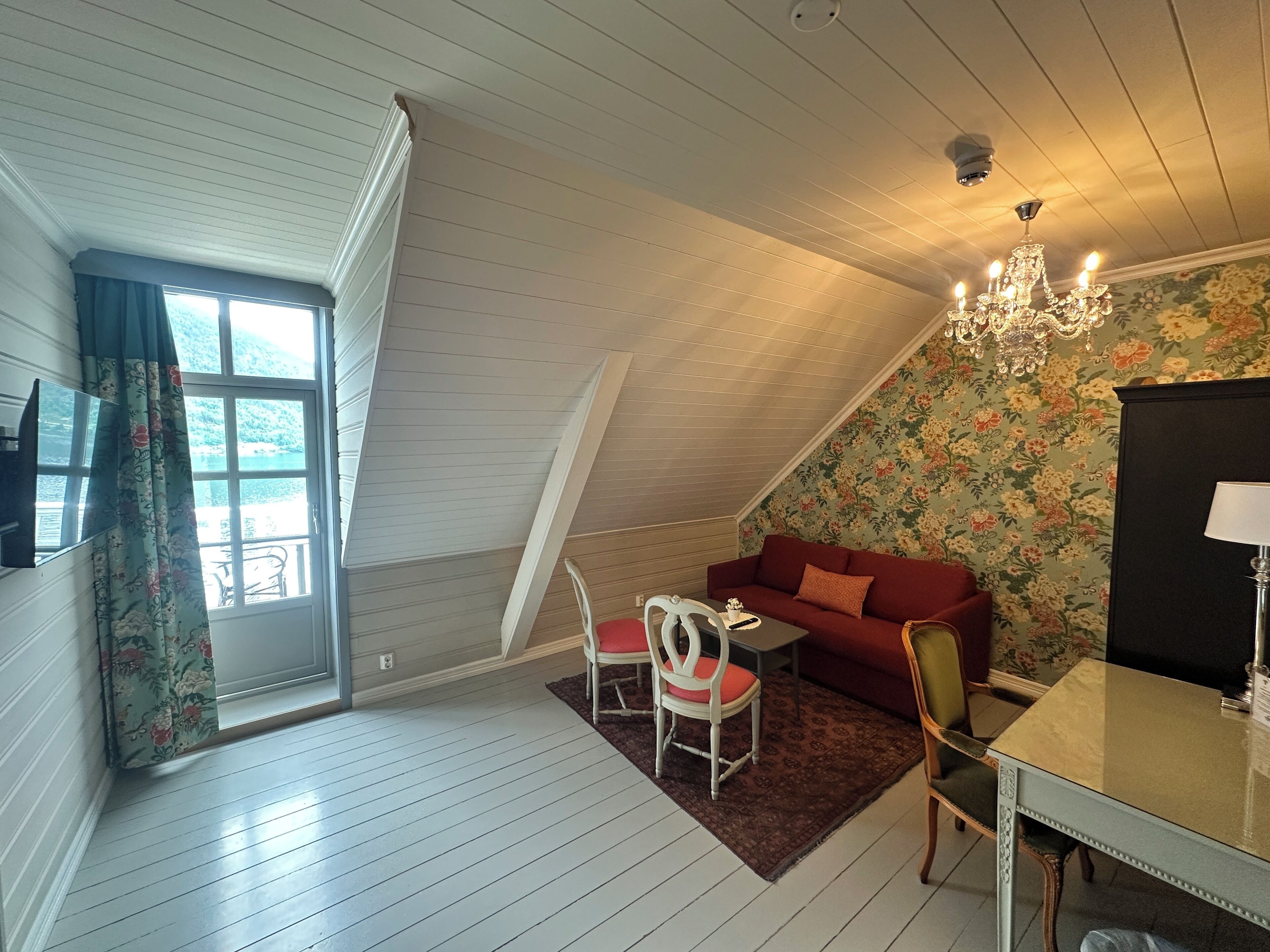 A cozy attic room with a red sofa, a small table, and a chandelier.
