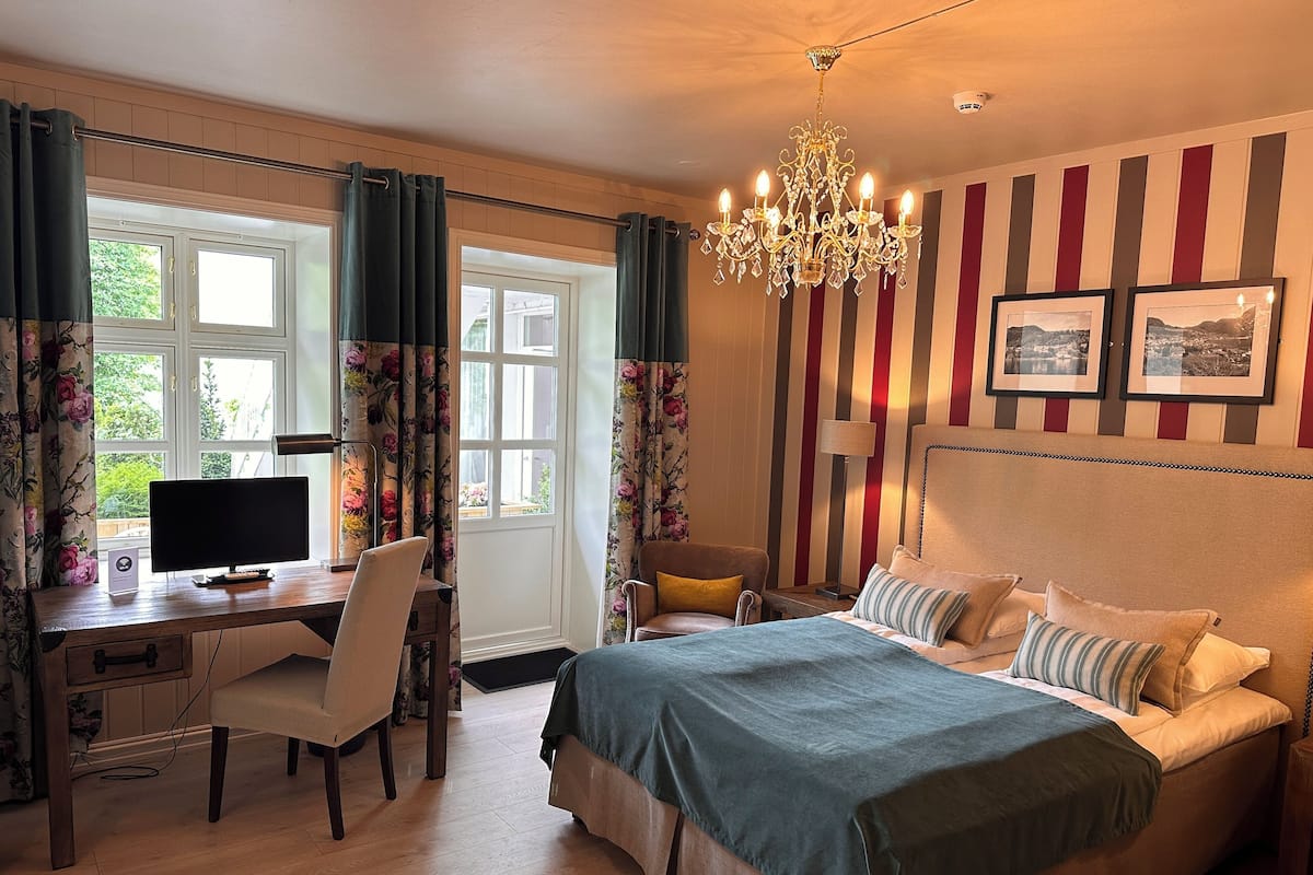 Un dormitorio con cama, escritorio con computadora, una silla, candelabro y papel tapiz a rayas.