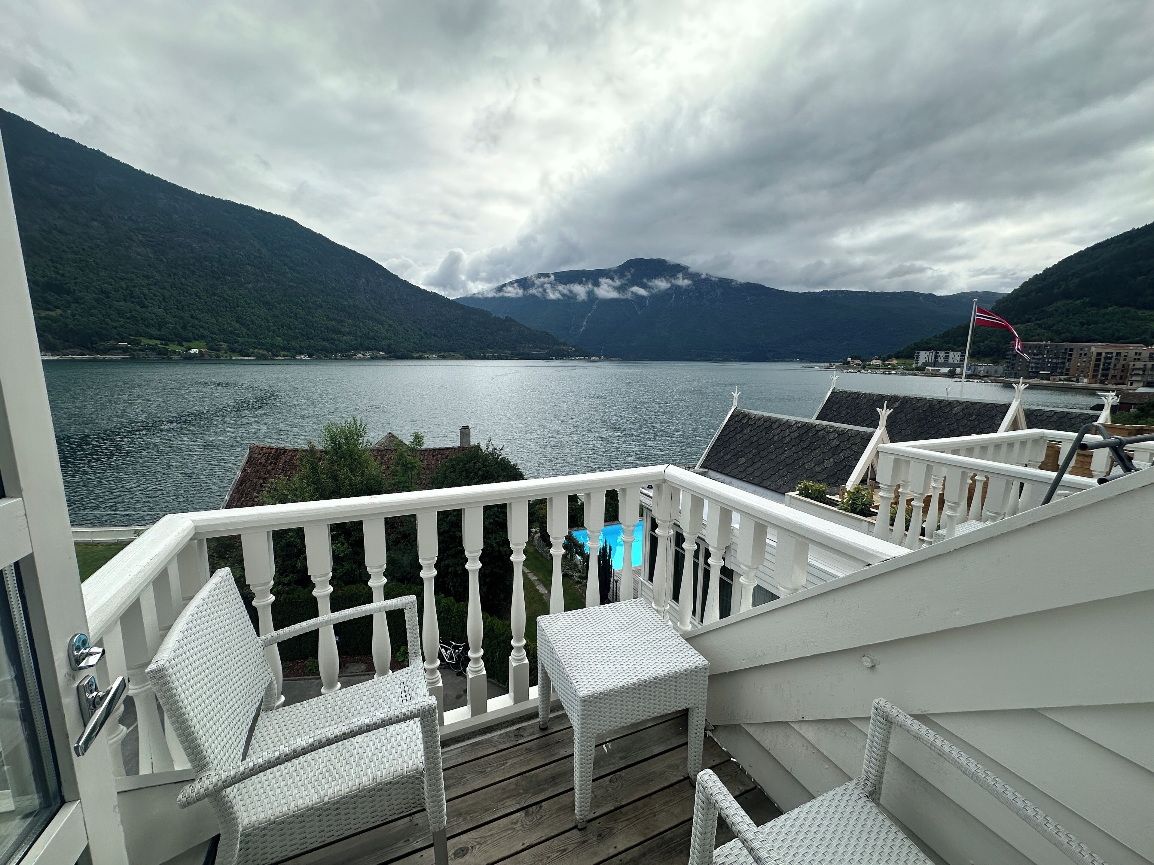 A balcony with wicker furniture overlooking a lake and mountains.