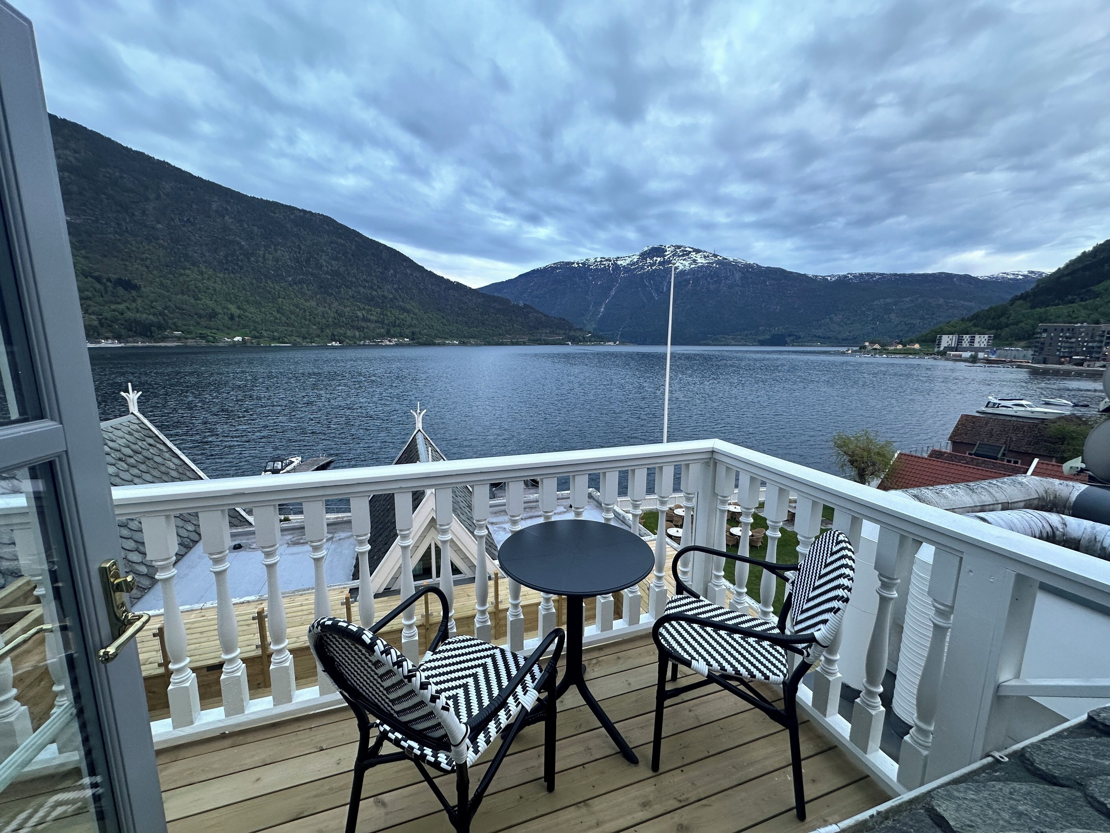 A balcony with two chairs and a table, overlooking a lake with mountains in the background.