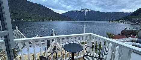A balcony with two chairs and a table, overlooking a lake with mountains in the background.