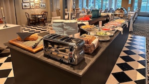 Een buffetgedeelte met een geruit vloertje, diverse gerechten en een zithoek met stoelen en tafels.