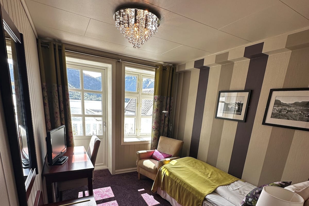Habitación de hotel con cama, escritorio, silla y vistas a las montañas a través del ventanal.