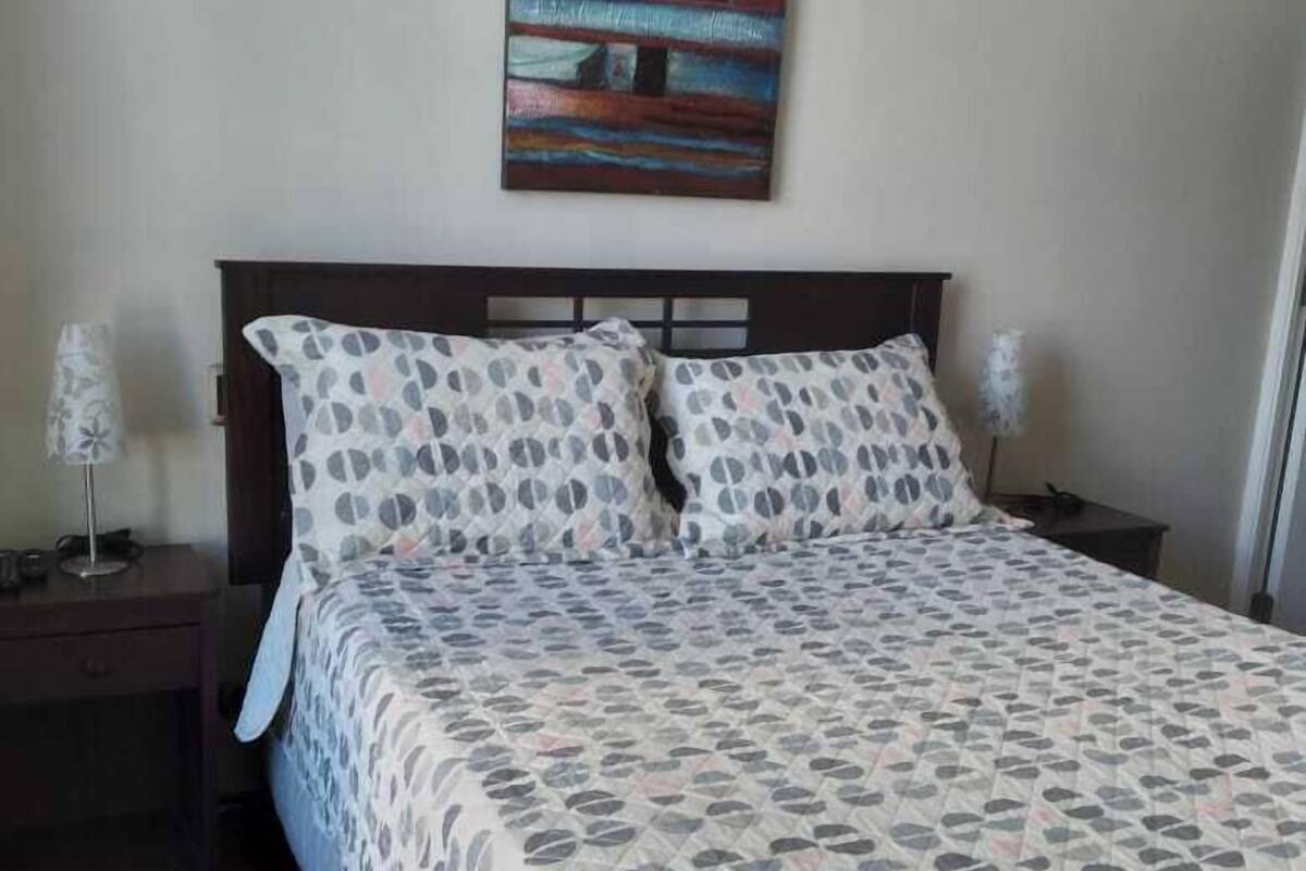 A bedroom with a bed, two nightstands, a lamp, and a painting on the wall.