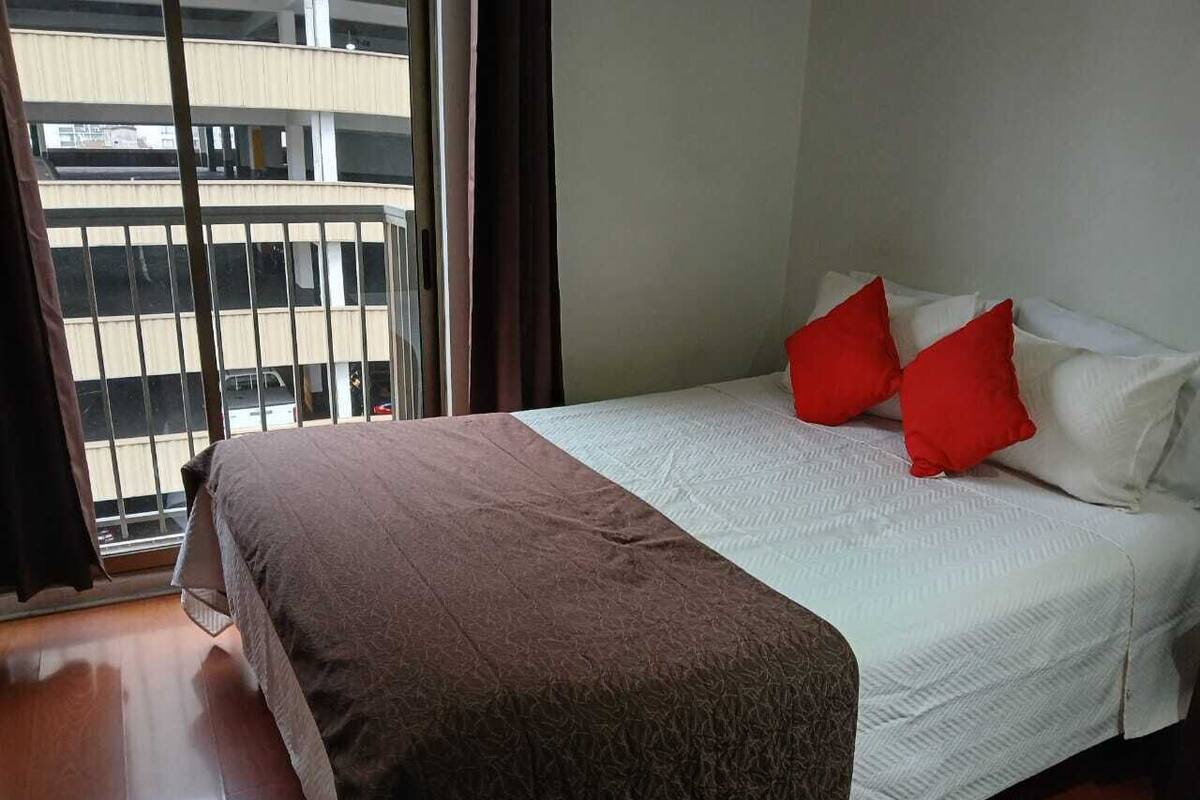 A hotel room with a bed, a window with a view of a building, and a curtain.