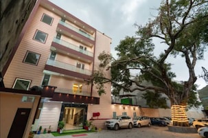 Un hotel de varios pisos con fachada moderna, una zona de estacionamiento y un gran árbol iluminado.