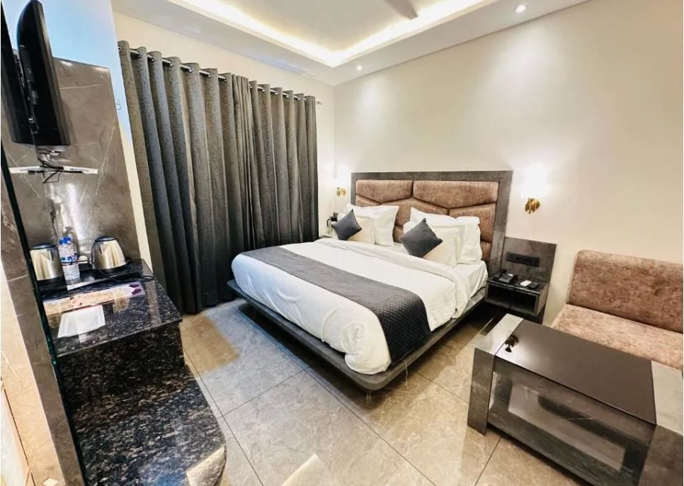 Una habitación de hotel moderna con una cama grande, un sofá, una mesa de centro, un televisor y un área de baño con ducha e inodoro.