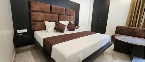 Quarto com cama grande, mesa de cabeceira, sofá e pequena mesa.