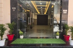 A hotel entrance with a glass door, a green artificial turf entrance mat, and potted plants on either side.