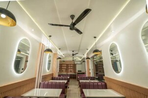 Interior de restaurante con cabinas, iluminación colgante, ventiladores de techo y paredes espejadas.